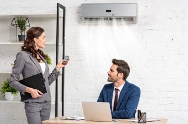 A woman holding a remote to a man sitting at a desk with an efficient air conditioning system.